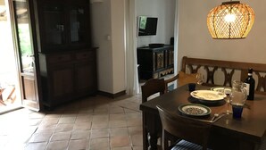 A dining area with a table set for two, a television mounted on the wall, and a decorative hanging light fixture. - Only ten minutes walk to the golf course and still very quiet (Saturnia)