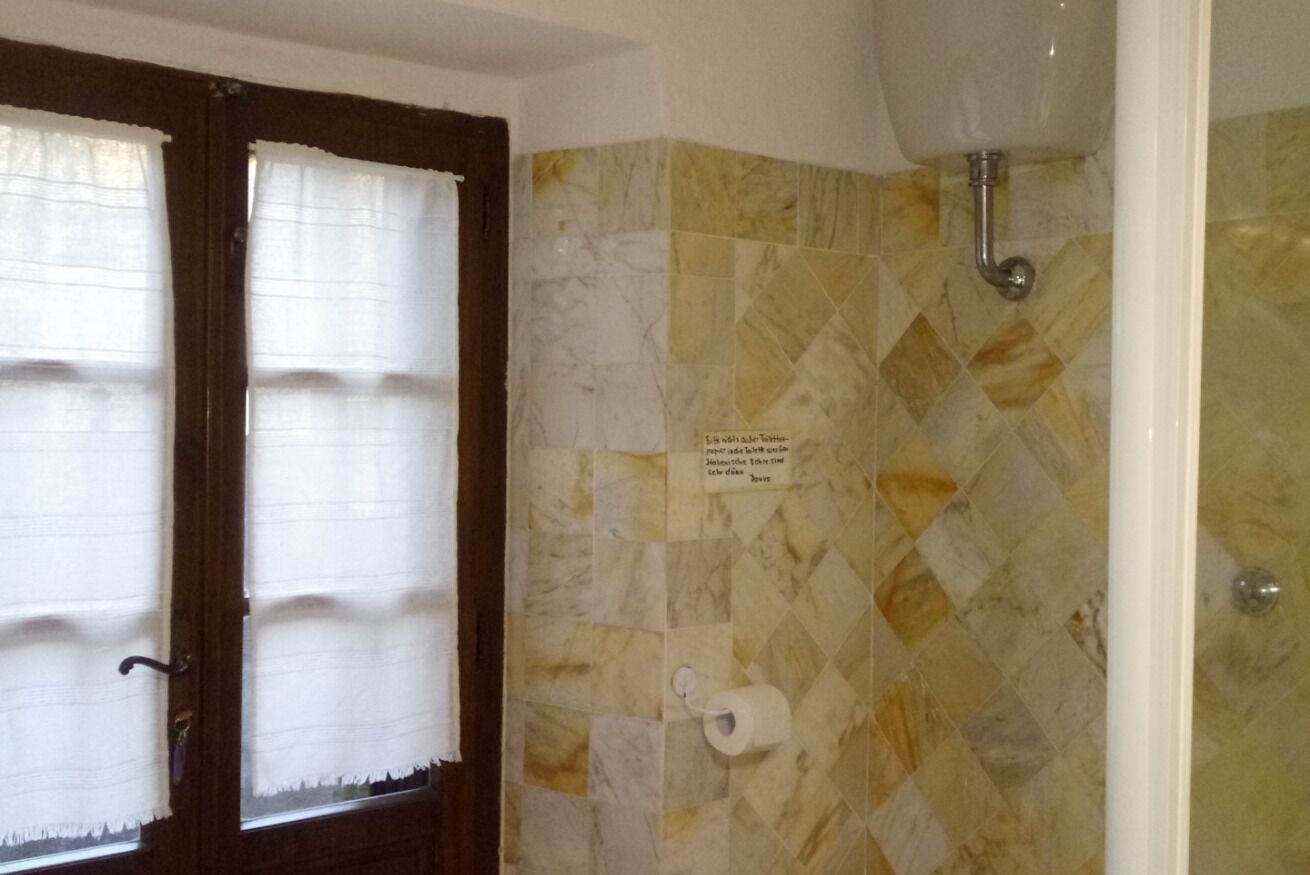 A bathroom with a tiled wall, a toilet paper holder, and a shower area.