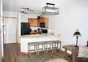 A modern kitchen with a central island, wooden cabinets, and a black refrigerator.