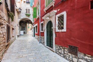 A narrow cobblestone street flanked by buildings with stone facades and green shutters. - Luxury Apartment Kastela Antika (Rovinj)