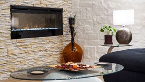 A modern living room with a stone wall, a fireplace, a glass coffee table with snacks, a dark sofa, and a potted plant.