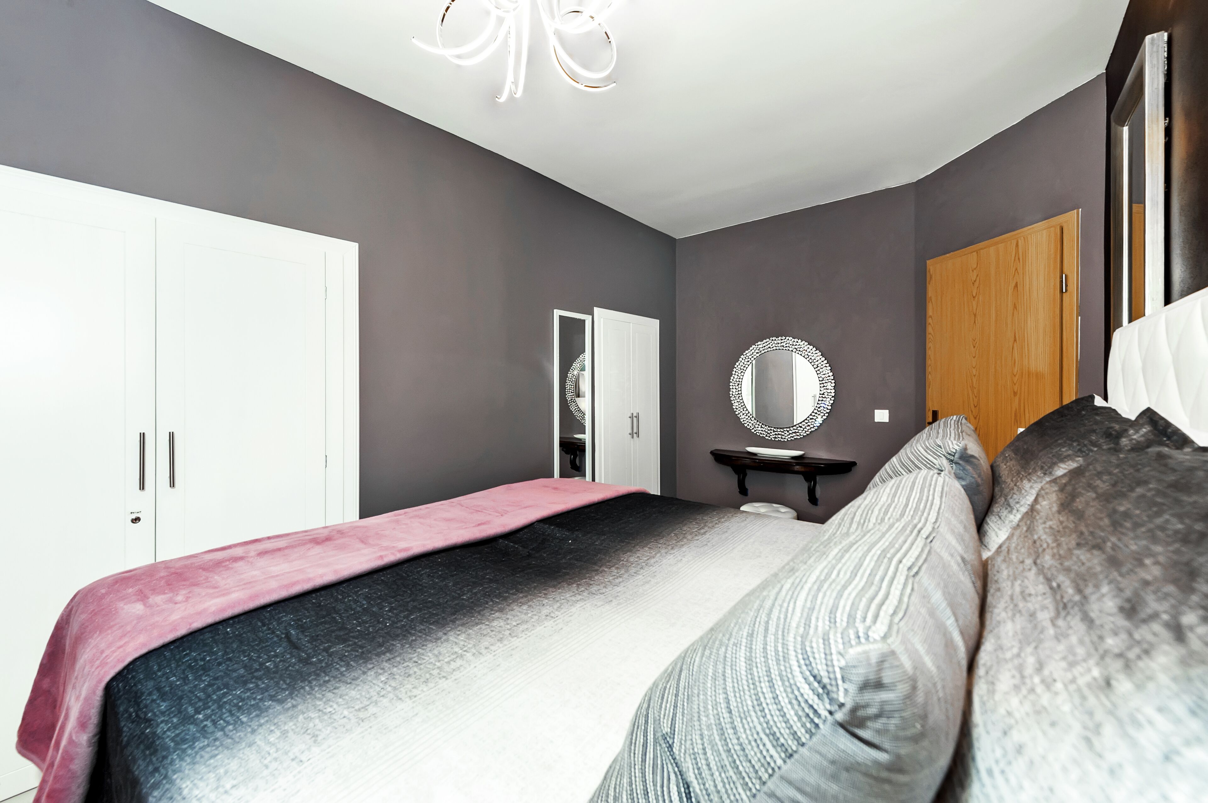 Un dormitorio con cama, mesita de noche, espejo, armario y puerta.