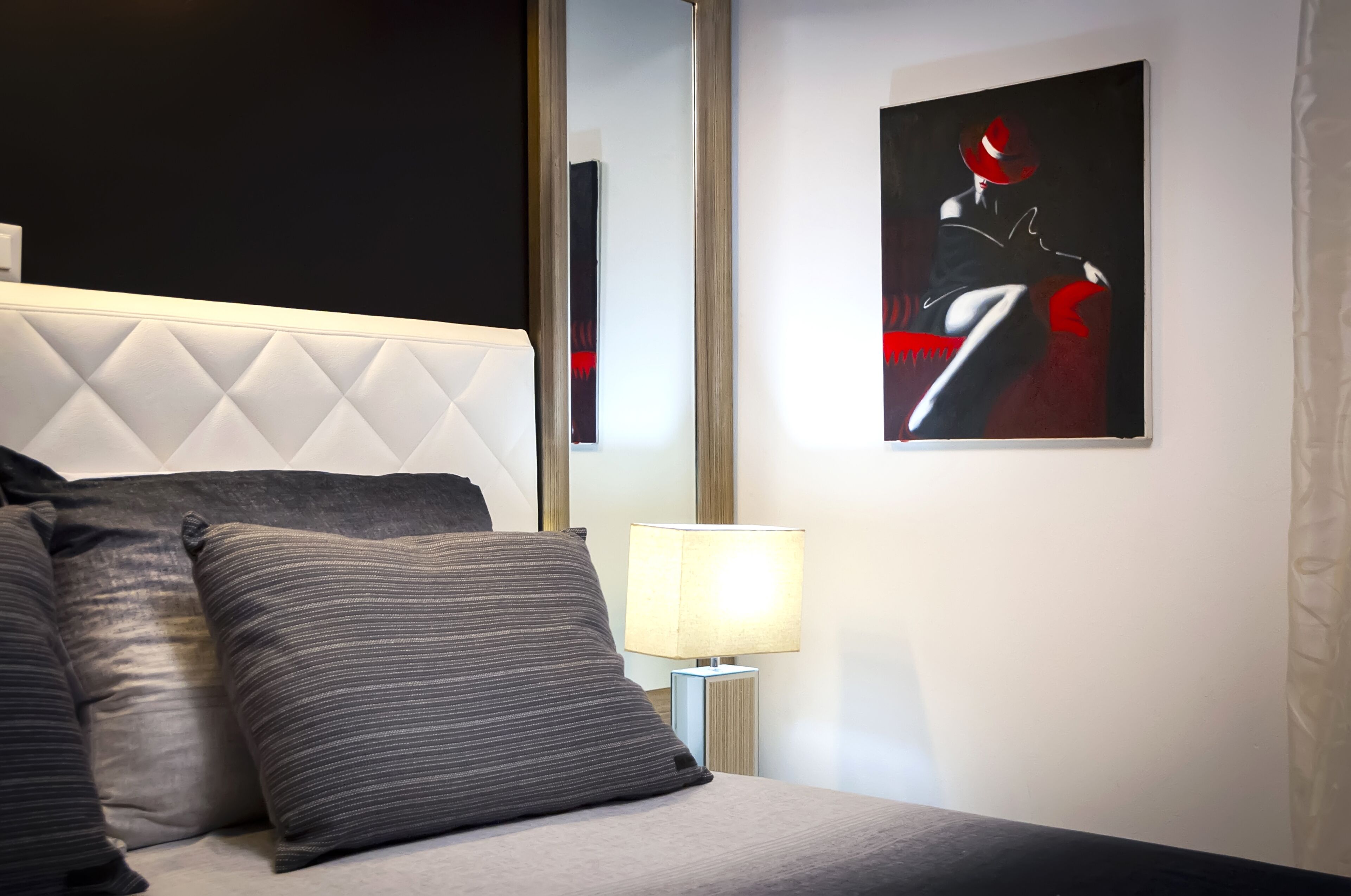 Une chambre d’hôtel moderne avec une tête de lit capitonnée, un grand tableau abstrait encadré, une lampe de chevet et une couvre-lit de couleur sombre.
