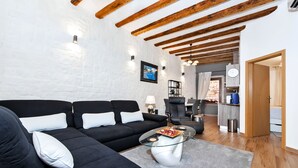 A modern living room with a black sectional sofa, a glass coffee table, and exposed wooden beams on the ceiling.