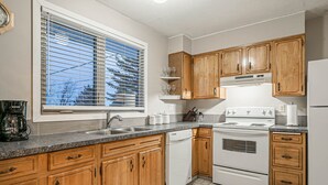 A kitchen with wooden cabinets, a white stove, a dishwasher, and a window with blinds. - Entire house, 6 BR/3BA, All Queen Beds, Central location  (Calgary)