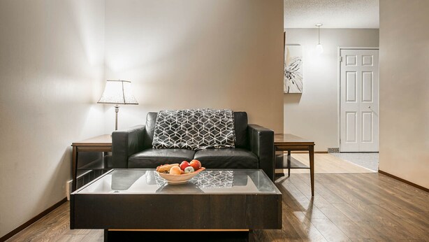 A living room with a glass coffee table, a black leather sofa with a patterned throw, a side table, a lamp, and a door in the background. - Entire house, 6 BR/3BA, All Queen Beds, Central location  (Calgary)