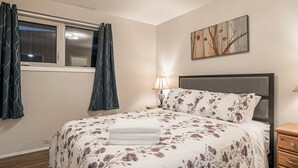 A bedroom with a bed, a nightstand, a lamp, a window with curtains, and a painting on the wall. - Entire house, 6 BR/3BA, All Queen Beds, Central location  (Calgary)