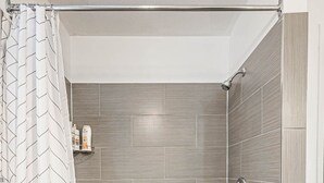 A modern bathroom with a freestanding bathtub, a showerhead, and a patterned shower curtain. - Entire house, 6 BR/3BA, All Queen Beds, Central location  (Calgary)
