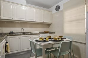 Una cocina con armarios blancos, encimera de granito, un lavabo y una mesa de comedor con sillas.