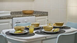 A kitchen with a dining table set for four, featuring yellow patterned bowls, plates, and a glass of orange juice. - Netos Apartment - By WeHostMadeira (Funchal)