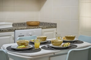 Una cocina con una mesa de comedor lista para cuatro personas, que incluye cuencos, platos y un vaso de jugo de naranja con diseños amarillos.