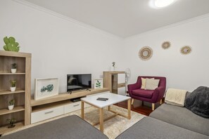 A modern living room with a flat-screen TV, a coffee table, a sofa, a red armchair, and a wooden entertainment unit with plants.