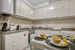 A modern kitchen with white cabinets, a built-in oven, a coffee maker, and a dining area with a table set for two.