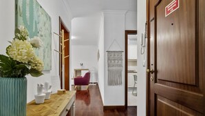A hallway with a wooden floor, a potted plant, a desk, a chair, and a door with a sign. - Netos Apartment - By WeHostMadeira (Funchal)