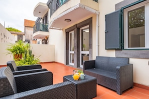 A patio area with wicker furniture, a table with a pitcher of orange juice, and a window with blinds.