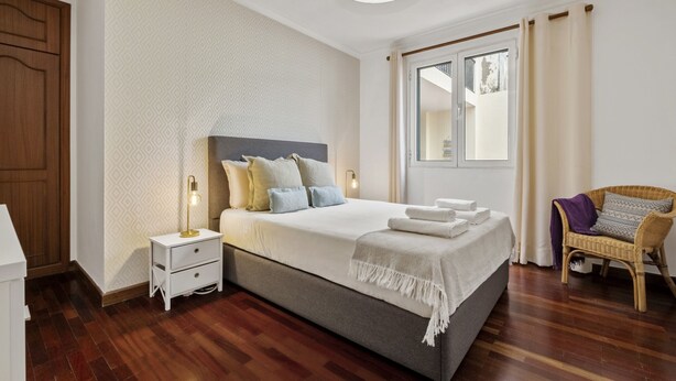 A neatly arranged bedroom with a bed, bedside lamps, a chair, and a window with curtains. - Netos Apartment - By WeHostMadeira (Funchal)