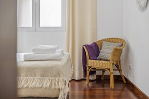 A room with a bed, a wicker chair, and a window with curtains.