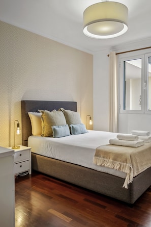 A modern bedroom with a large bed, bedside lamps, and a mirror. - Netos Apartment - By WeHostMadeira (Funchal)