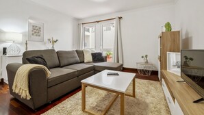 A modern living room with a grey sectional sofa, a white coffee table, a TV stand with a flat-screen TV, and a small side table with a plant. - Netos Apartment - By WeHostMadeira (Funchal)