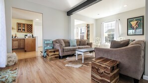 A spacious living room with a sofa, a coffee table, and a wooden chest. A kitchen is visible in the background.