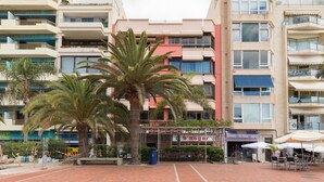 A multi-story hotel with balconies, a central courtyard with palm trees, and outdoor seating. - Huge Balcony over Las Canteras By CanariasGetaway (Las Palmas de Gran Canaria)