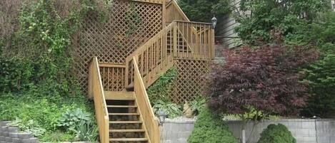 A wooden outdoor staircase with a lattice railing, surrounded by greenery and a small garden area.