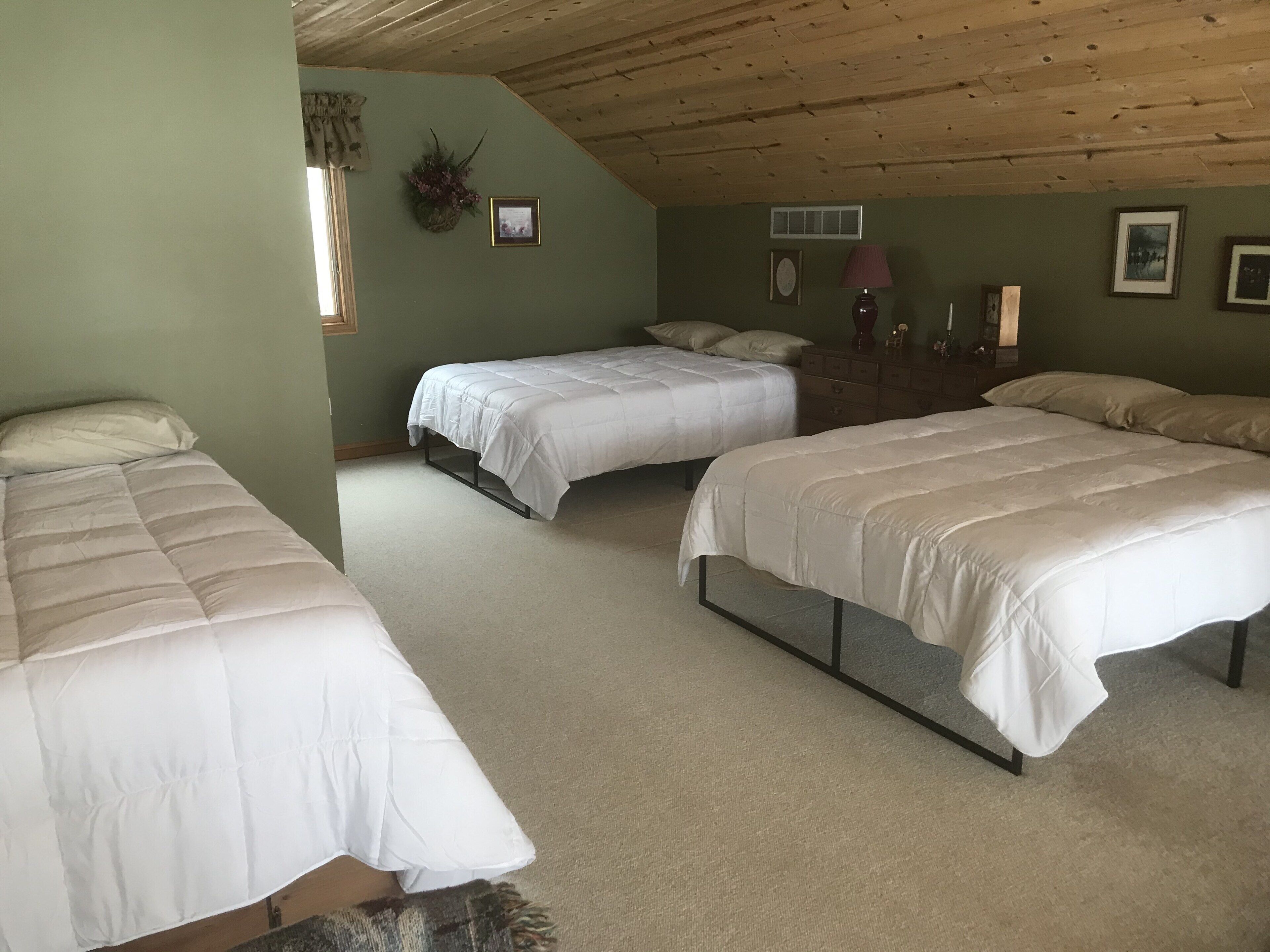 A bedroom with three beds, a wooden ceiling, and a green wall.