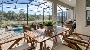 Un patio cubierto con piscina, mesa y sillas de madera, y una zona de barbacoa.