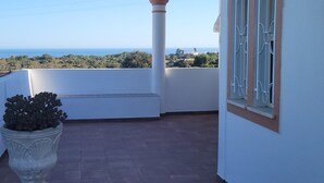 Eine überdachte Terrasse mit Blick auf das Meer, ein Blumentopf und ein Gebäude mit Ziegeldach und weißen Wänden.