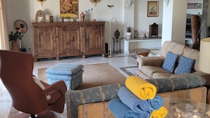 Ein Wohnzimmer mit einer Couch, einem Sessel, einem Hocker, einem Holzschrank und einem Kamin.