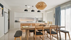 A modern kitchen with white cabinets, a central island, and a dining area with wooden chairs and a bench.
