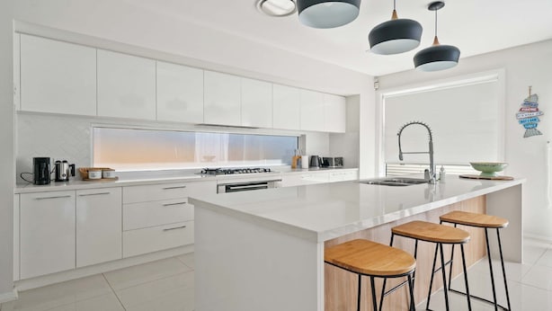 A modern kitchen with white cabinetry, a central island with bar stools, a gas stove, and pendant lighting.