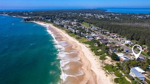 An aerial view of a coastal residential area with houses along the beach, a road, and a large body of water.