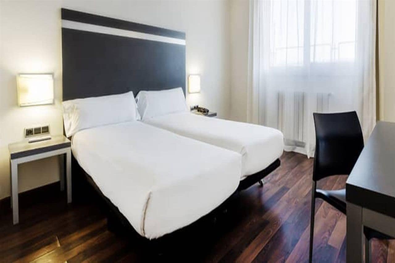 A hotel room with two beds, a desk, and a chair.