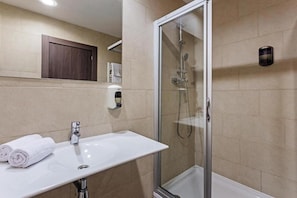 Un baño moderno con un lavamanos blanco, una cabina de ducha con paredes de vidrio y un mueble de madera sobre el espejo.