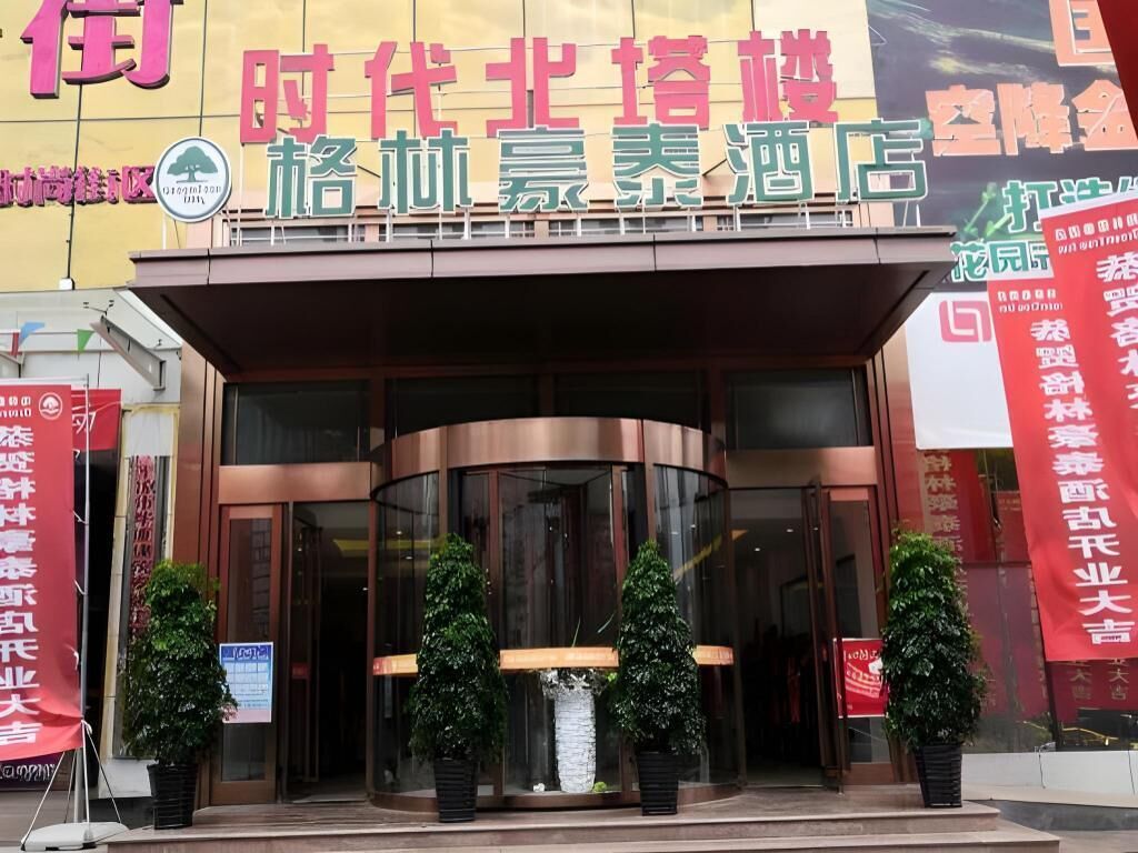 A hotel entrance with a curved facade, large glass doors, and potted plants in front.