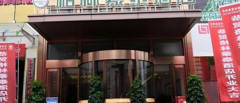 A hotel entrance with a curved facade, large glass doors, and potted plants in front.