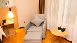 Et moderne hotelværelse med en grå sofa, et lille bord med en servietæller og et sengebord med lampe og telefon.