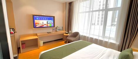A hotel room with a bed, a desk, a chair, a television, and a window with curtains.