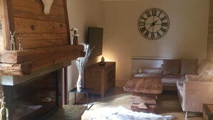 A cozy living room with a fireplace, a clock on the wall, and a sofa. - ANCELLE Chalet-style house 160 m2 at the foot of the slopes (Ancelle)
