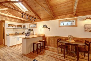 Et træinteriør med et køkken og spiseområde, med træbjælker, en central ø og et spisebord med stole.