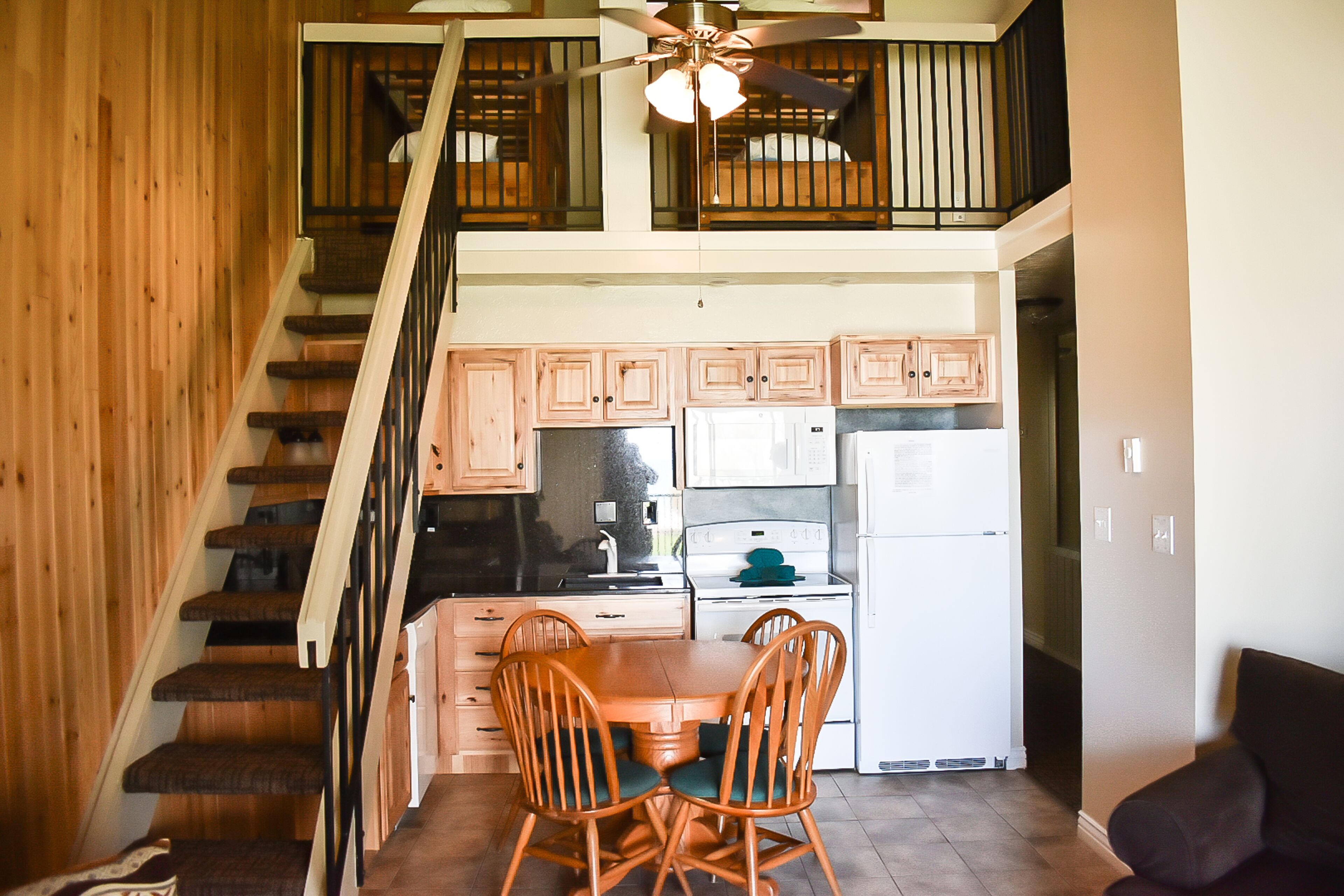 A kitchen with wooden cabinets, a dining table with chairs, and a staircase leading to an upper level.
