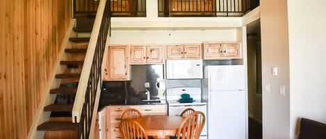 A kitchen with wooden cabinets, a dining table with chairs, and a staircase leading to an upper level.