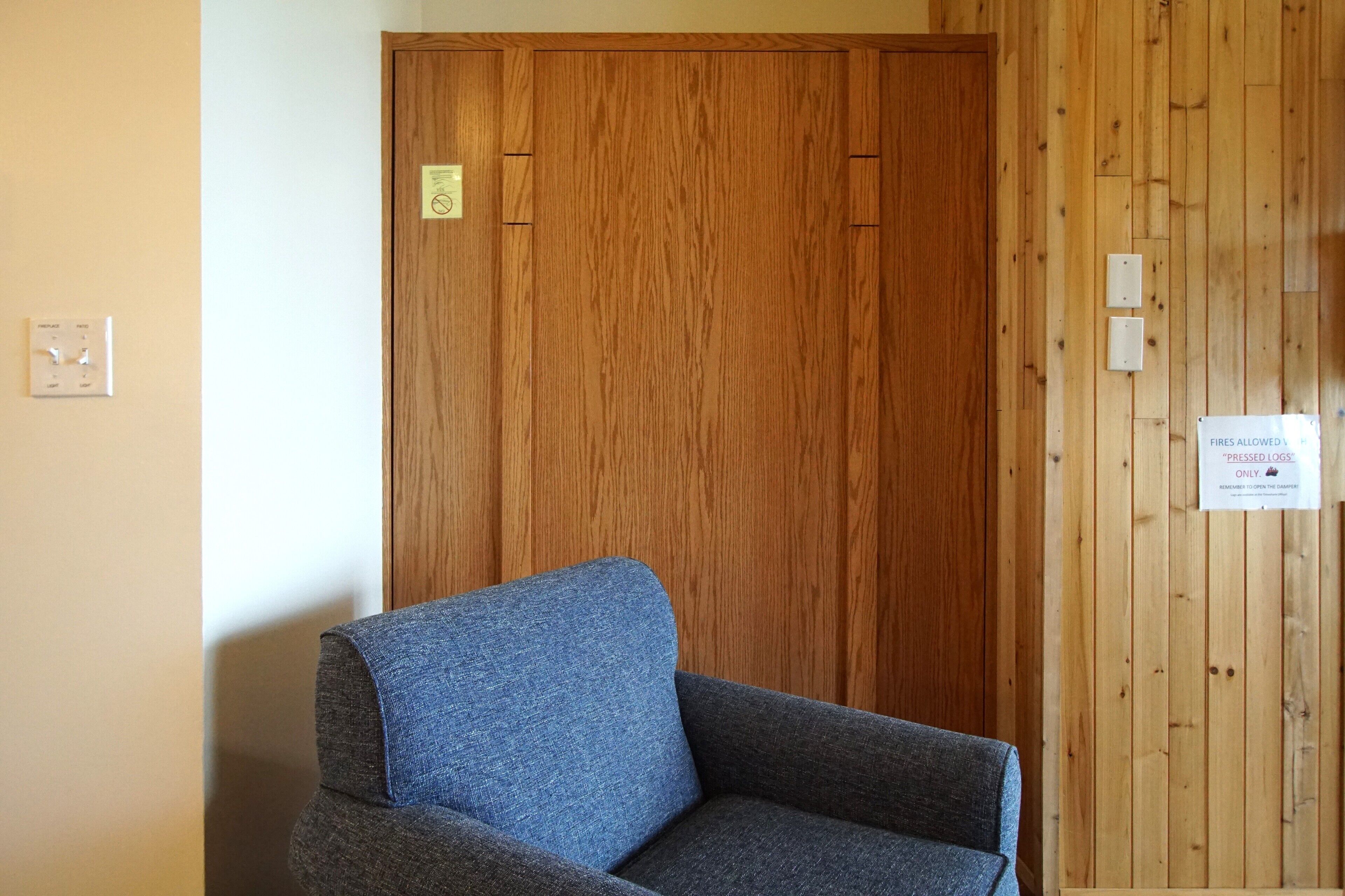 A room with a wooden wardrobe, a grey sofa, and a sign indicating 'FIRES ALLOWED'.