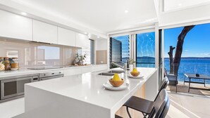 A modern kitchen with a central island, stainless steel appliances, and a view of the sea. - Baydream on the Beach - With Breathtaking Water Views (Corlette)