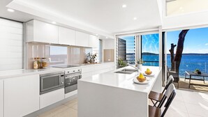 A modern kitchen with a large island, built-in appliances, and a view of the sea. - Baydream on the Beach - With Breathtaking Water Views (Corlette)
