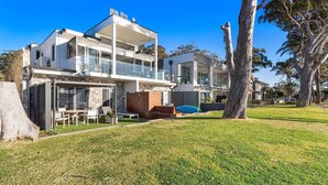 A modern two-story house with a balcony, a stone wall, and a grassy yard. - Baydream on the Beach - With Breathtaking Water Views (Corlette)