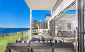 Ein moderner Balkon mit Meerblick, eine Essecke mit Tisch und Stühlen sowie ein Wohnbereich mit Sofa und Couchtisch.