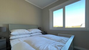 Un lit bien fait, avec du linge de lit blanc, dans une pièce dotée d’une grande fenêtre, d’une table de chevet et d’une lampe.