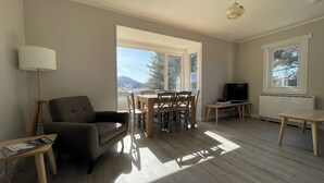 Un salon comprenant un canapé, une table à manger avec des chaises, un téléviseur posé sur un meuble et un radiateur.